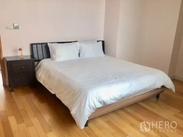Condominium for rent in Khlong Toei, Bangkok - Spacious master bedroom with white bedding, bedside table and wooden floors.
