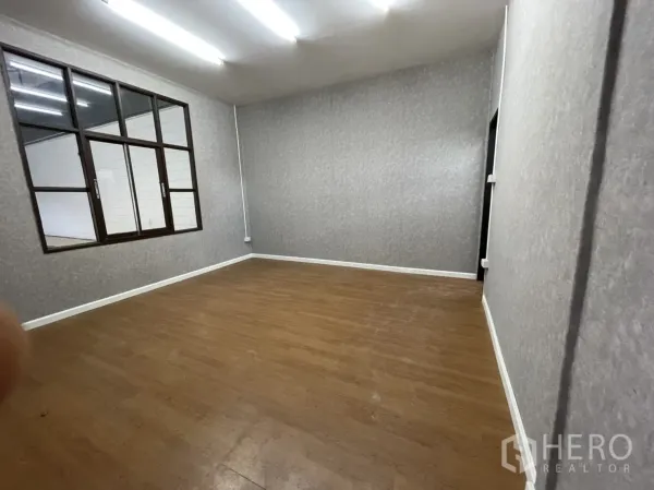 Warehouse for rent in Lam Luk Ka, Pathum Thani - Private office room with wood-style flooring, grey textured walls and an internal window overlooking the warehouse.
