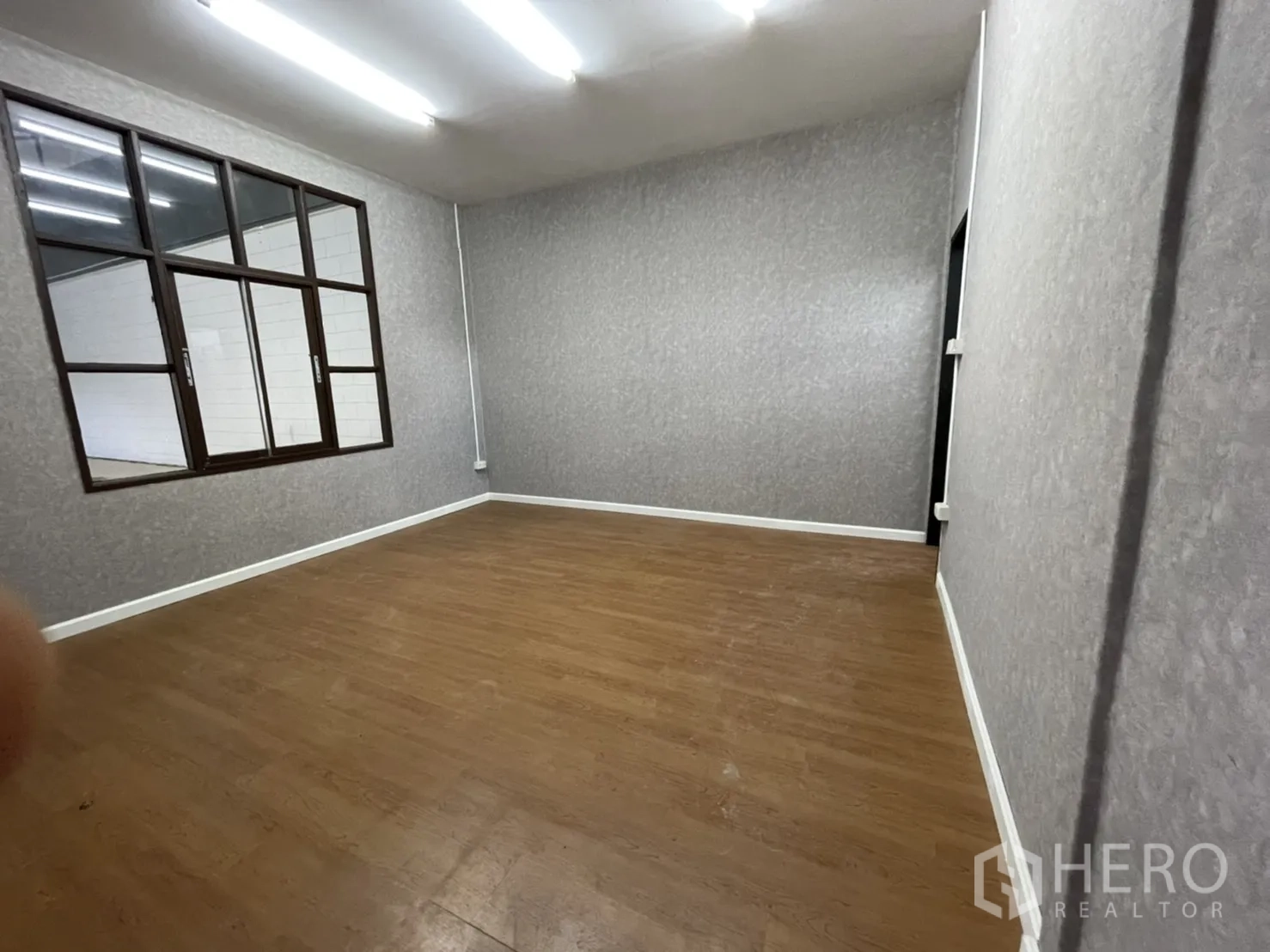 Warehouse for rent in Lam Luk Ka, Pathum Thani - Private office room with wood-style flooring, grey textured walls and an internal window overlooking the warehouse.