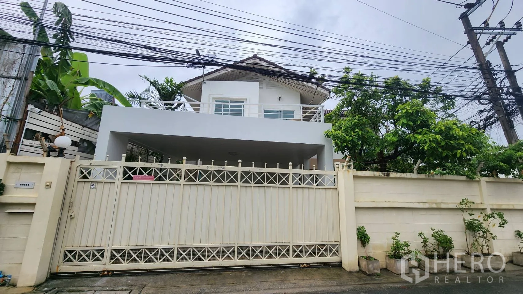 Detached House for rent in Watthana, Bangkok - Front facade with gated entrance, covered carport, and balcony.