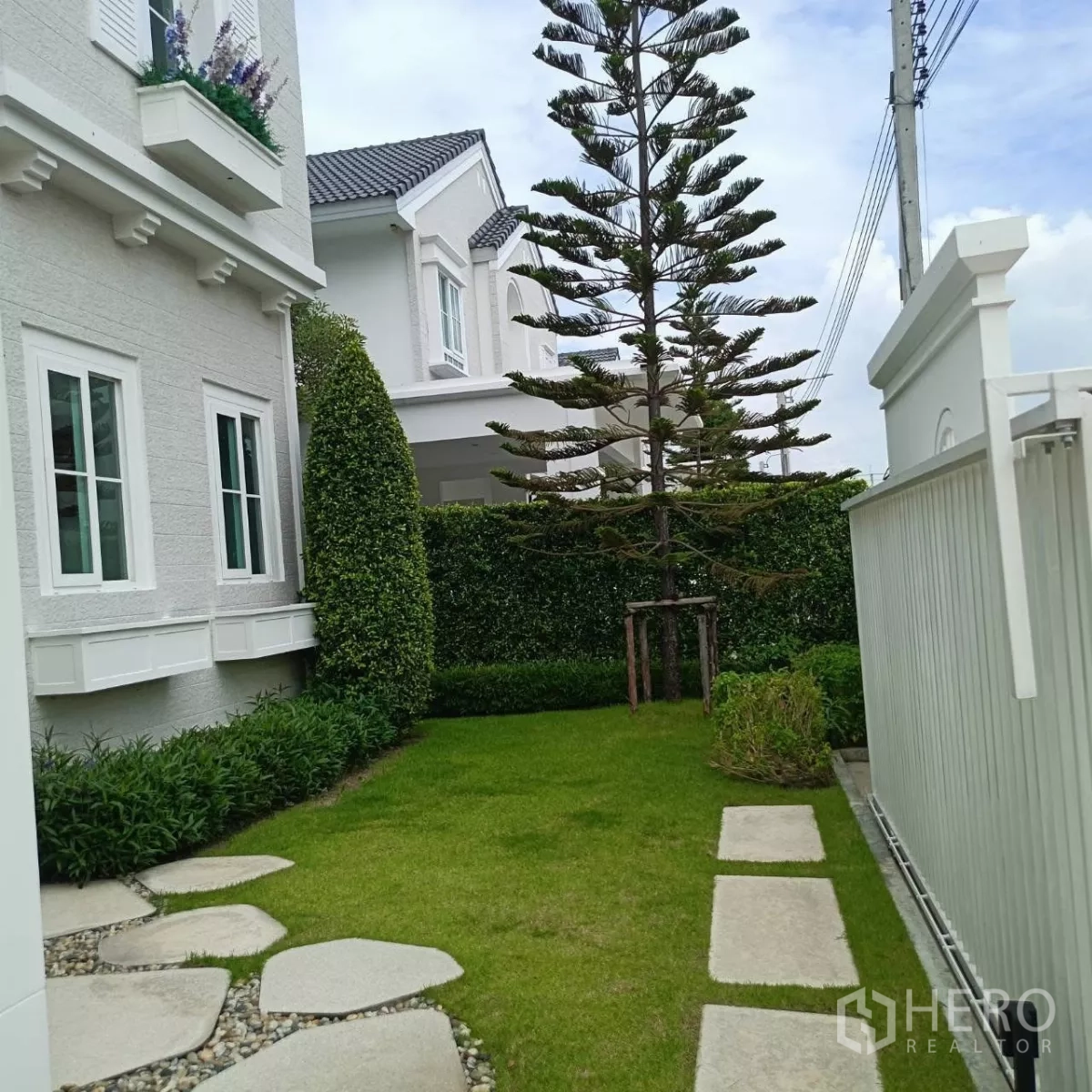 Detached House for rent in Bang Phli, Samut Prakan - Side garden with stepping stones, manicured hedges and a tall pine next to the home.