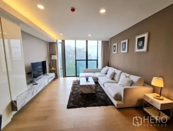 Condominium for rent in Khlong Toei, Bangkok - Spacious living area with floor‑to‑ceiling windows, sofa, TV console and recessed lighting.