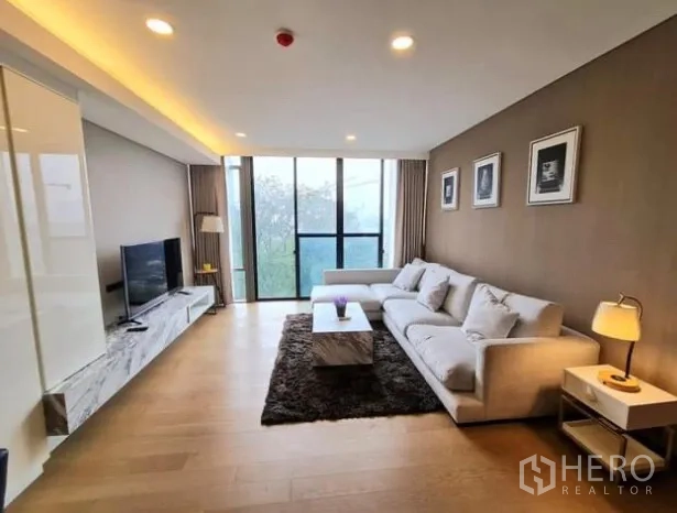Condominium for rent in Khlong Toei, Bangkok - Spacious living area with floor‑to‑ceiling windows, sofa, TV console and recessed lighting.