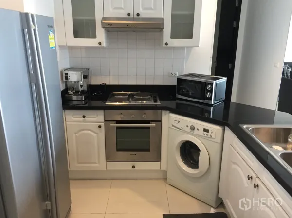 Condominium for rent in Ratchathewi, Bangkok - U-shaped kitchen with black granite tops, built-in oven and hob, washing machine, and stainless double-door fridge.