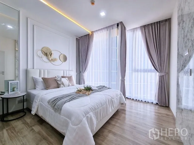 คอนโด ขาย - ห้องนอนรับแสงเต็มบาน ม่านโปร่ง และชุดเครื่องนอนสีขาว