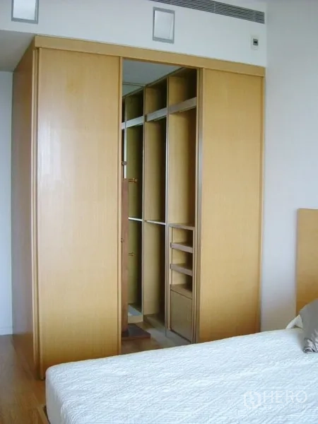 Condominium for rent in Sathon, Bangkok - Bedroom with built-in wooden wardrobe featuring sliding doors and open shelving.