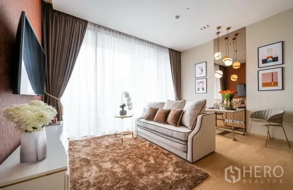 Condominium for rent or sale in Bang Rak, Bangkok - Cozy lounge with plush rug, sheer curtains and modern media console beside a large window.