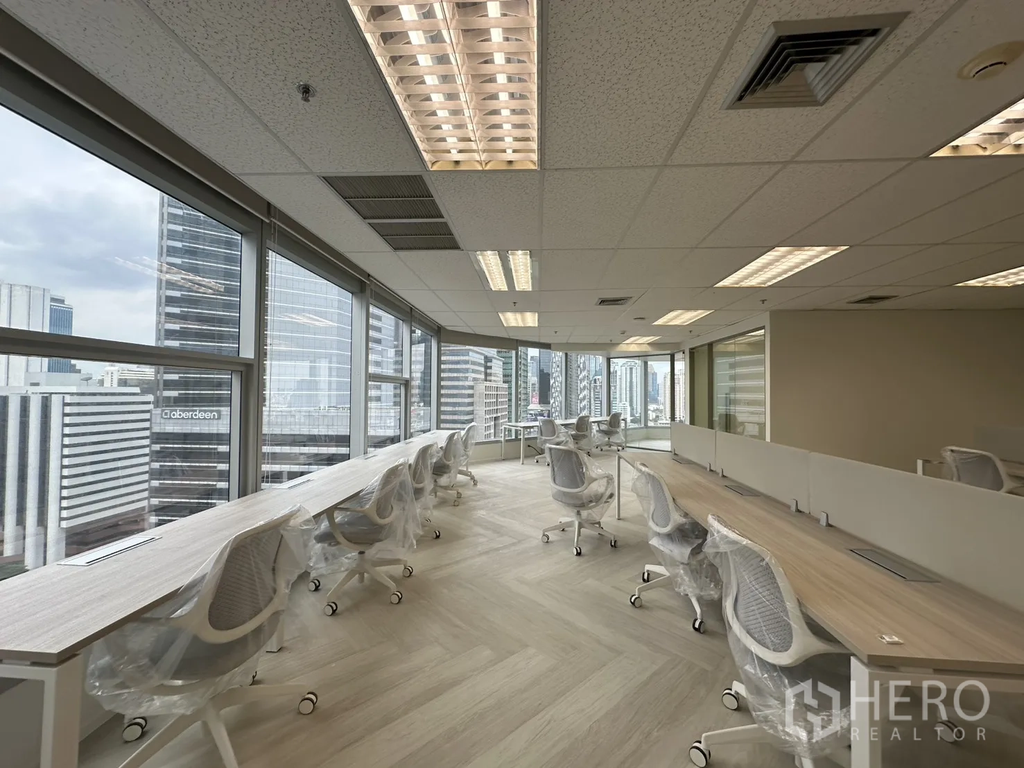 办公室 for rent in Sathon, Bangkok - 窗边长条工位眺望天际线，上方为荧光灯照明。