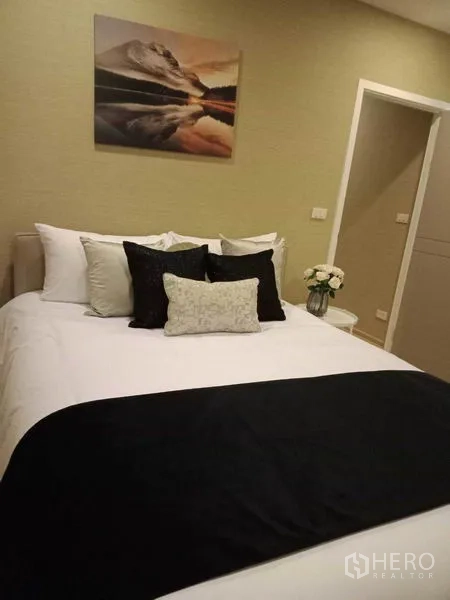Townhouse for rent or sale in Suan Luang, Bangkok - Bedroom with crisp white bedding, a black throw, wall art and a doorway to an ensuite.