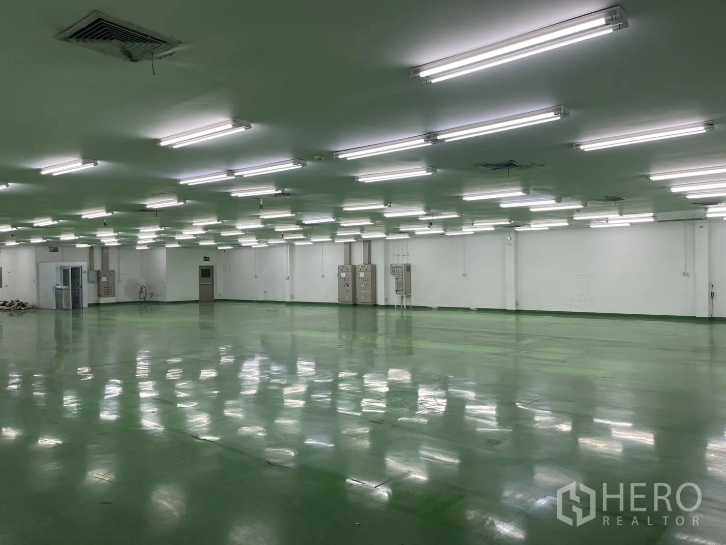 工厂 for rent in Mueang Samut Prakan, Samut Prakan - 低天花的大型厂房，绿色环氧地坪、明亮日光灯、白色墙面与电控柜。
