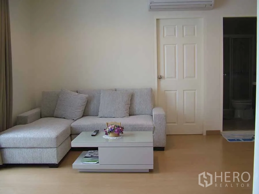 公寓 出租或出售在Watthana, Bangkok - 曼谷วัฒนา区两卧公寓明亮客厅，灰色L形沙发、茶几与壁挂空调。