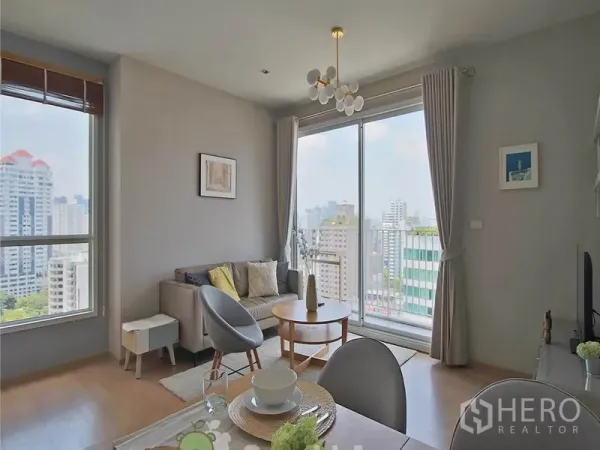 Condominium for rent or sale in Khlong Toei, Bangkok - Living area with floor-to-ceiling windows and city skyline views from the balcony.