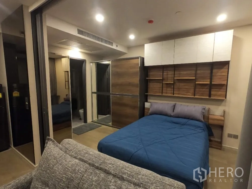 คอนโด for rent in Watthana, Bangkok - ห้องนอนอบอุ่น ผ้านวมสีน้ำเงิน โซฟาปลายเตียง ตู้เสื้อผ้าบานกระจก และทางเข้าห้องน้ำ