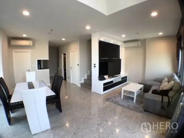 Condominium for rent in Khlong Toei, Bangkok - Open-plan living and dining room with TV wall, sectional sofa and polished floors.