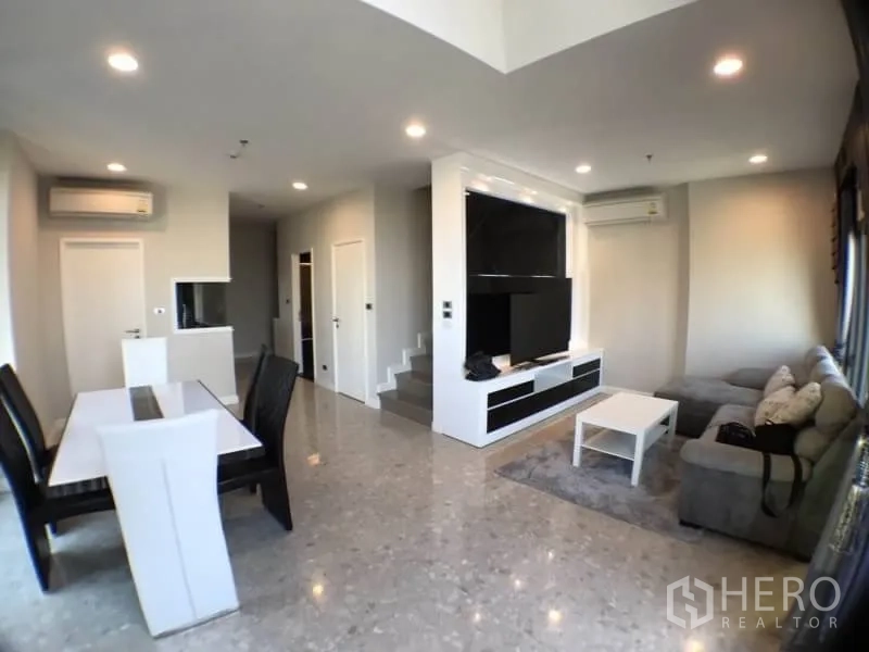 Condominium for rent in Khlong Toei, Bangkok - Open-plan living and dining room with TV wall, sectional sofa and polished floors.
