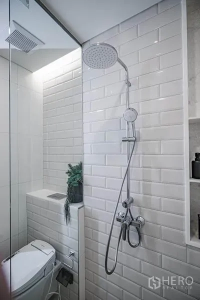 Condominium for sale in Khlong Toei, Bangkok - Bathroom corner featuring a rain shower and handheld sprayer set against glossy white subway tiles.