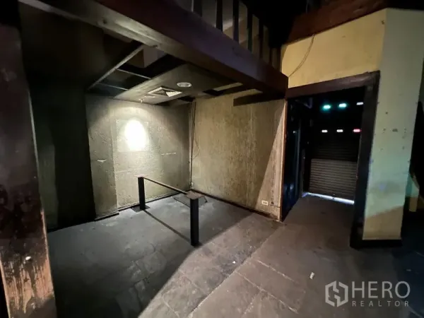 Shophouse for sale in Bang Rak, Bangkok - Dim ground-floor interior with concrete flooring, mezzanine beams and a shuttered entrance.