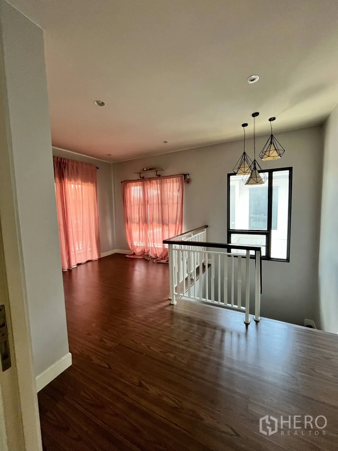 Detached House for rent or sale in Lam Luk Ka, Pathum Thani - Upstairs family area with pendant lights, railing and pink curtains.