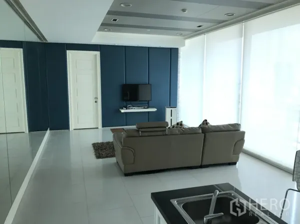 公寓 出租在Watthana, Bangkok - 宽敞客厅，落地窗与卷帘，从厨房中岛望向电视。
