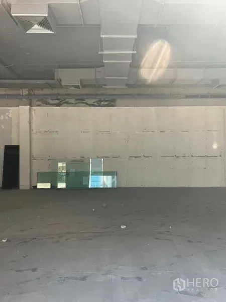 Retail Space for rent in Khlong Toei, Bangkok - Open-plan retail floor facing a blank wall with stacked glass panels beneath a ducted ceiling.
