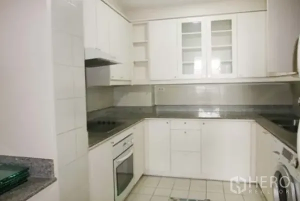 Condominium for rent in Sathon, Bangkok - Closed U‑shaped kitchen with white cabinets, granite countertops, electric hob, oven and washing machine.