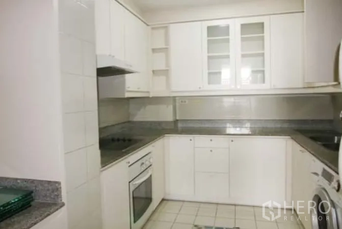 Condominium for rent in Sathon, Bangkok - Closed U‑shaped kitchen with white cabinets, granite countertops, electric hob, oven and washing machine.