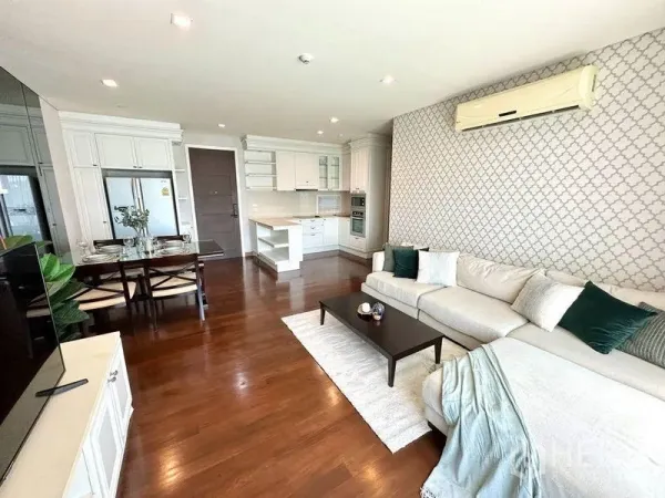 Condominium for rent in Watthana, Bangkok - Open-plan living room with L-shaped sofa, wooden floors, and a white built-in kitchen in a Thonglor-area condo.