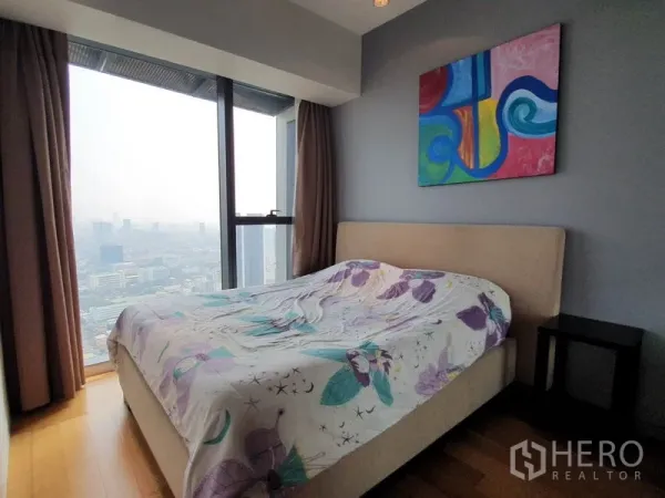 Condominium for rent in Sathon, Bangkok - Cozy bedroom with bed and colorful artwork, featuring a tall city-view window.