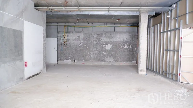 Retail Space for rent in Watthana, Bangkok - Wide retail bay with structural column, visible utility lines and concrete walls prepared for renovation.