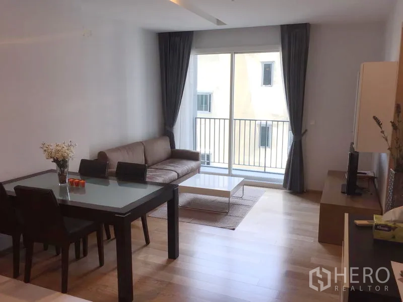Condominium for rent in Khlong Toei, Bangkok - Living and dining area with sofa set, dining table and sliding door to a small balcony.
