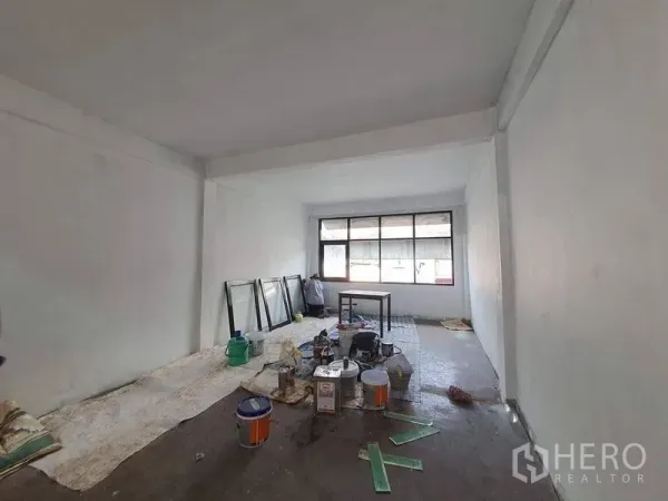 Shophouse for rent in Bangkok - Deep open-plan interior with wide window and assorted renovation tools and paint cans.