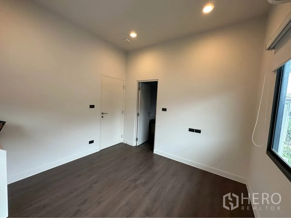 Detached House for rent in Bang Kapi, Bangkok - Empty room with dark wood flooring, recessed ceiling lights, and window.