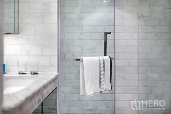 Condominium for rent in Bang Rak, Bangkok - Modern bathroom featuring a marble vanity and a glass-enclosed shower with white subway tiles.
