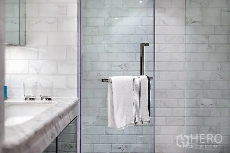Condominium for rent in Bang Rak, Bangkok - Modern bathroom featuring a marble vanity and a glass-enclosed shower with white subway tiles.