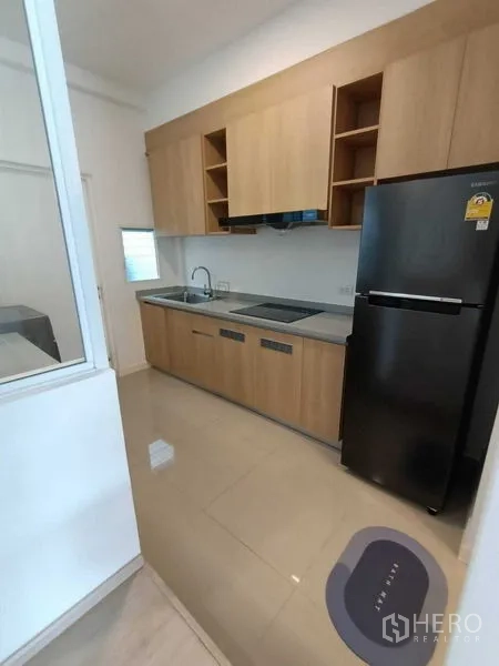 联排别墅 出租在Prawet, Bangkok - 走廊式厨房，浅色木柜、灶台、水槽与黑色冰箱。