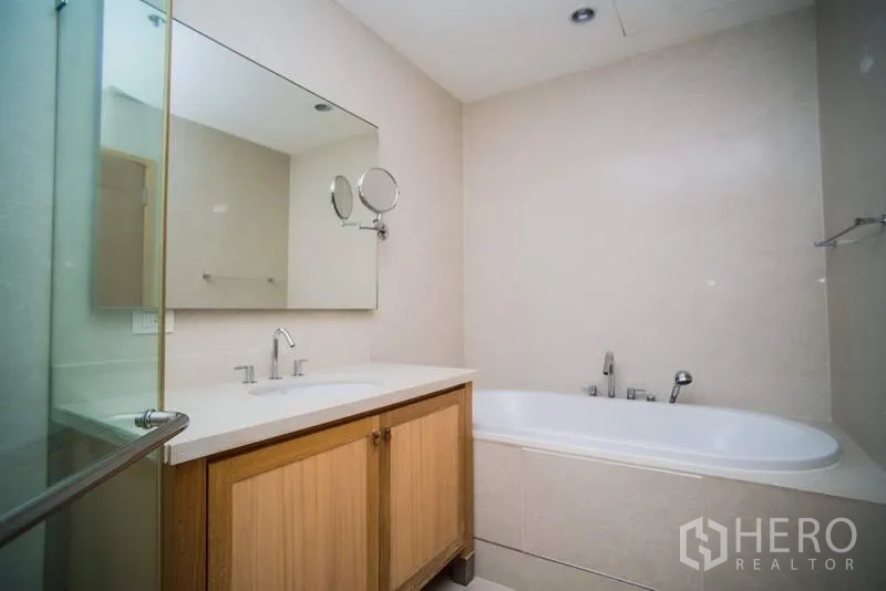 Condominium for rent or sale in Khlong Toei, Bangkok - Modern bathroom featuring a vanity with mirror and a built-in bathtub.