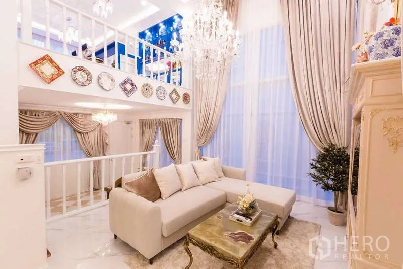 Townhouse for rent in Lat Phrao, Bangkok - Double-height living room with chandelier, mezzanine and floor-to-ceiling curtains.