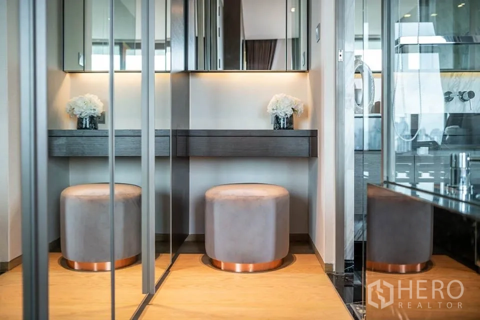 Condominium for rent or sale in Bang Rak, Bangkok - Dressing area with mirrored wardrobes, soft lighting and round stools at a makeup vanity.