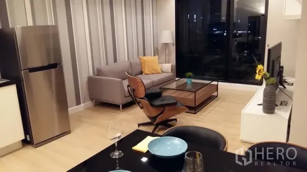 公寓 出租在Sathon, Bangkok - 夜景客厅，灰色沙发、条纹特色墙与通向阳台的落地玻璃。