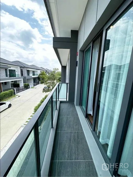 独立式住宅 出租或出售在Bang Phli, Samut Prakan - 玻璃栏杆的长阳台，俯瞰宁静的小区街景。