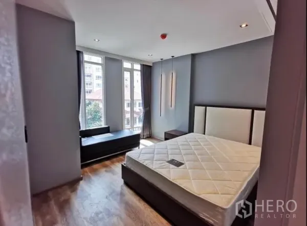 Condominium for rent in Sathon, Bangkok - Primary bedroom with large windows, upholstered bed and city and tree views.