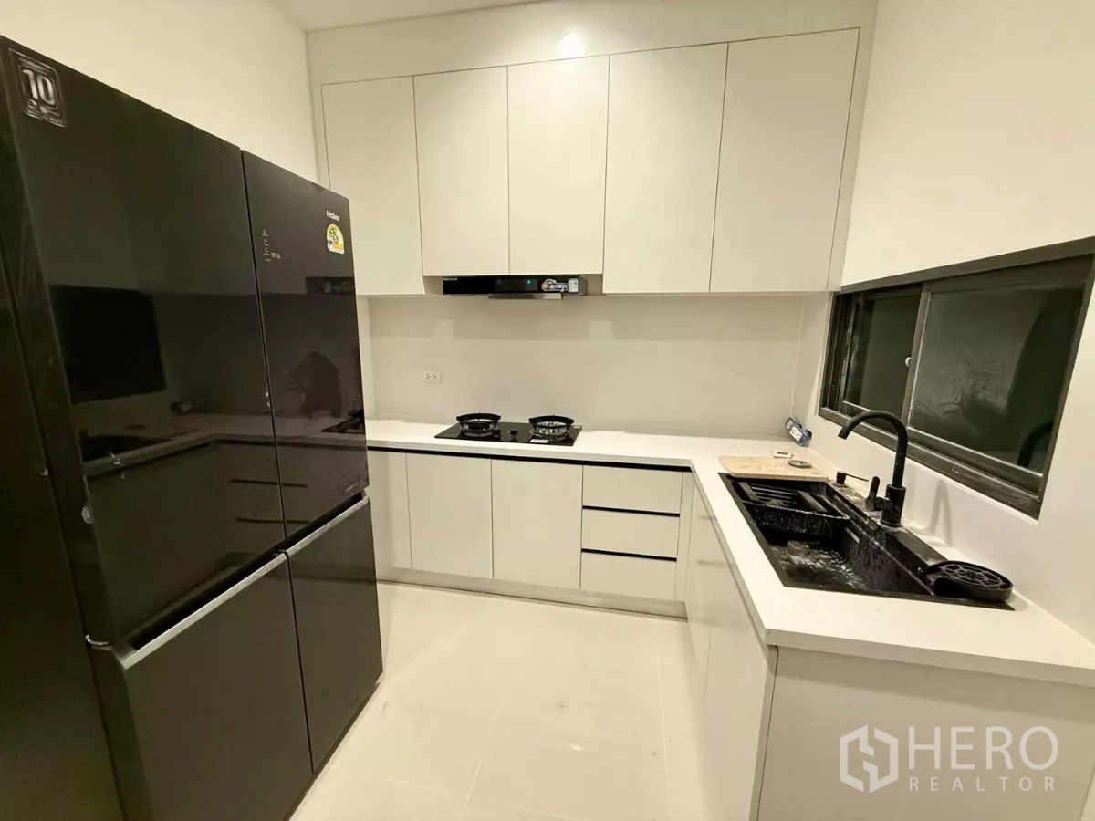 独立式住宅 出租在Bang Phli, Samut Prakan - 封闭式L形厨房，黑色双门冰箱、燃气灶与白色柜体。