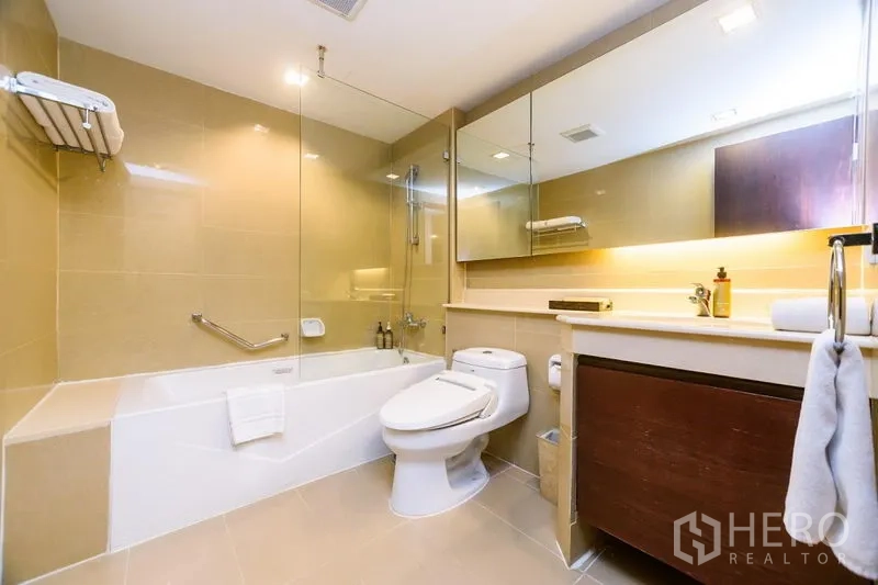 Condominium for rent in Khlong Toei, Bangkok - Modern bathroom with bathtub, glass shower screen, large mirror and long vanity countertop.