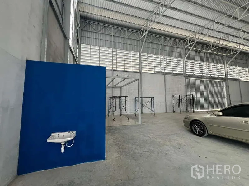 货栈 出租在Prawet, Bangkok - 室内角落，墙挂洗手盆、蓝色办公室隔断与脚手架，钢梁屋顶。