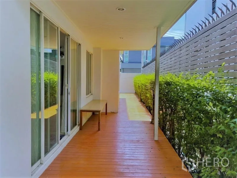 独立式住宅 出租在Suan Luang, Bangkok - 侧边有顶木质露台，推拉落地窗与修剪整齐的绿篱。