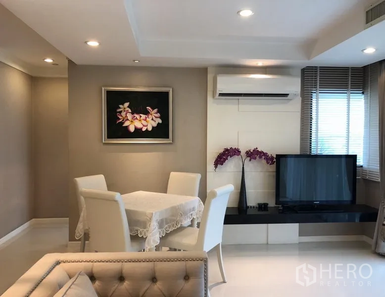 Condominium for rent or sale in Sathon, Bangkok - Cozy dining corner beside TV console and wall-mounted air conditioner with floral artwork.