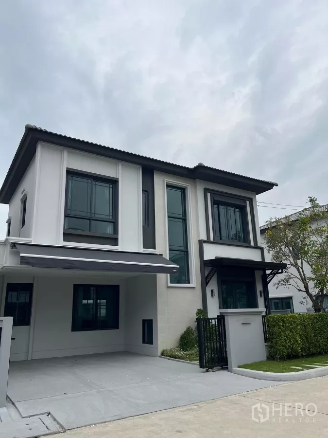 Detached House for rent or sale in Bang Phli, Samut Prakan - Angled view of the contemporary house exterior showing the driveway, entry gate, and trimmed hedge.