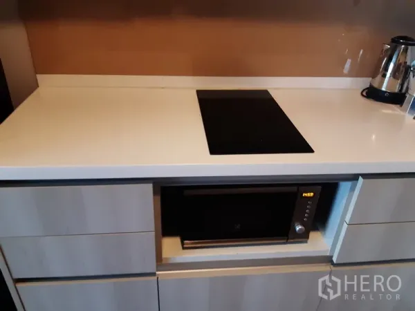 Condominium for rent in Khlong Toei, Bangkok - White countertop with induction cooktop and built-in microwave below.