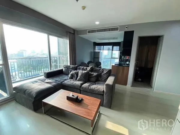 公寓 出售在Huai Khwang, Bangkok - 转角客厅，落地窗与L型沙发，阳台眺望城市天际线。