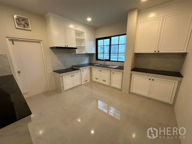 Detached House for rent or sale in Bang Phli, Samut Prakan - Bright built‑in kitchen with white cabinetry, black countertops, tiled floors and a window over the sink.
